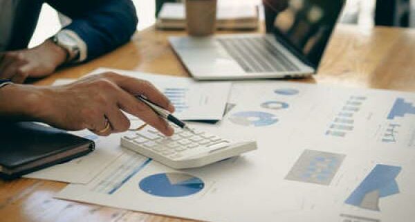 A woman sits at a desk with a calculator and sheets of data spread across it.